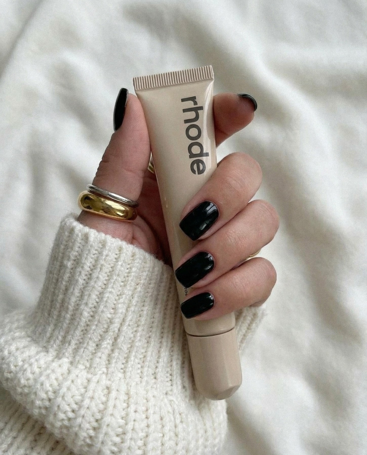 RHODE Lip Treatment in einer Hand mit schwarzer Maniküre